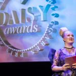 Dam med kub på huvudet står framför stor logotyp DAISY BEAUTY AWARDS